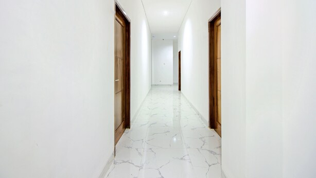 Un pasillo con paredes blancas y piso de mármol, que conduce a una puerta al final.