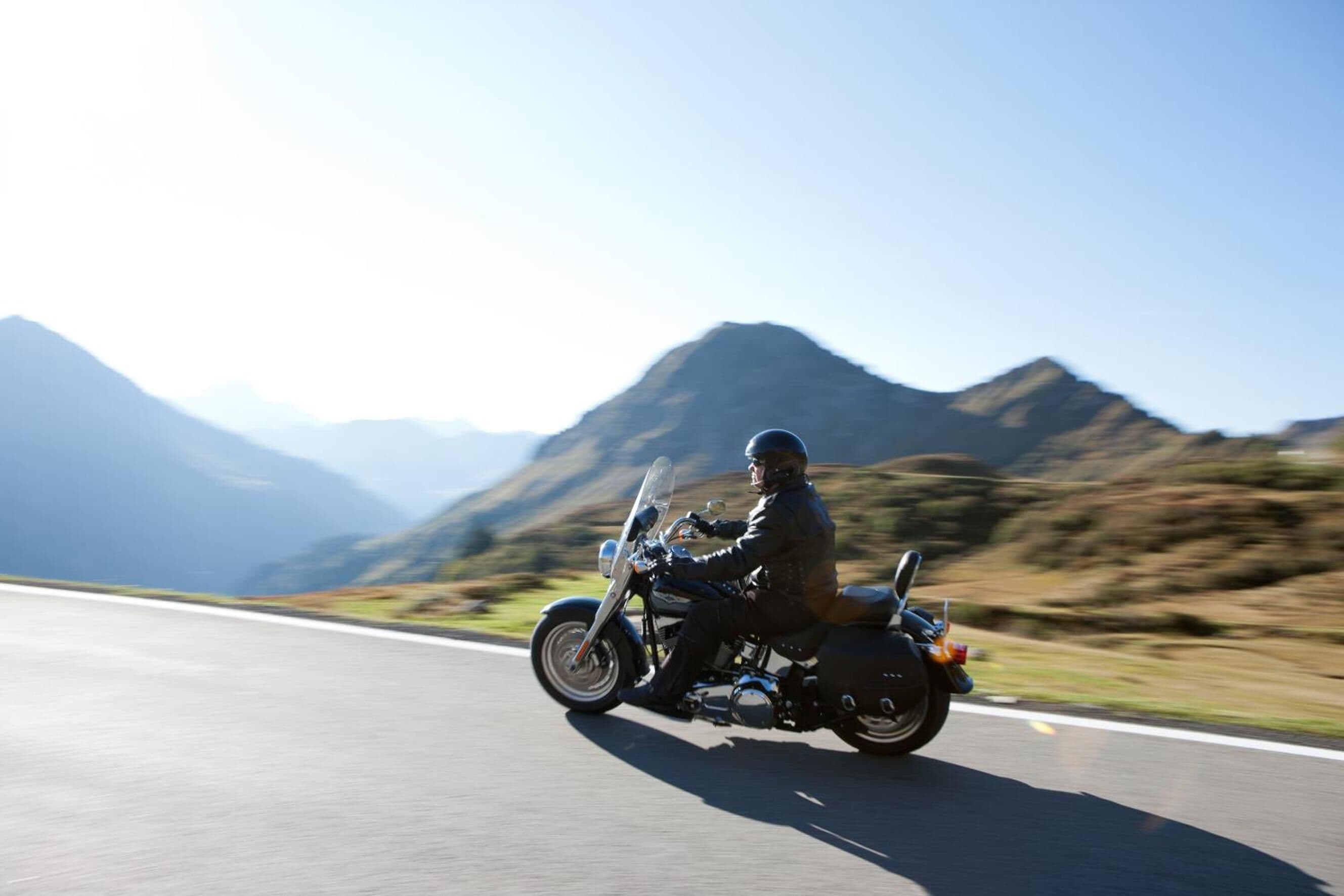 A motorcycle rider on a road with mountainous terrain in the background.