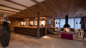 A cozy interior with a wooden ceiling, a central bar area, seating arrangements, and a fireplace. - Hotel Walliserstube (Damüls)