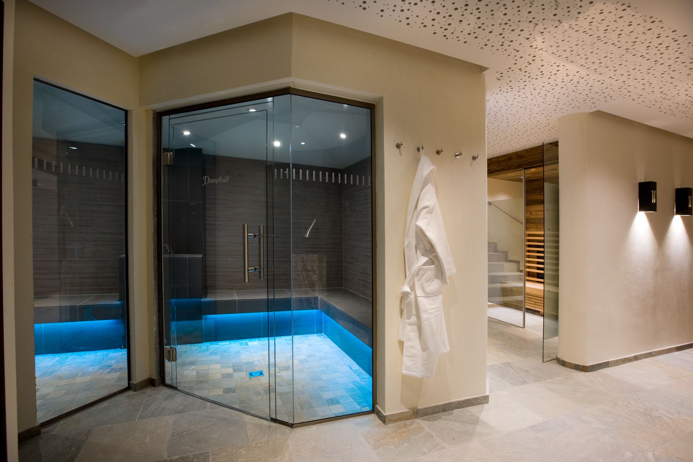 A modern bathroom with a glass-enclosed shower, a visible tiled floor, and a wooden staircase in the background.