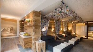 A modern spa area with wooden paneling, a large sofa, and a ceiling with a colorful fabric design. - Hotel Walliserstube (Damüls)