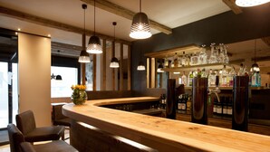 A bar area with wooden bar counter, hanging pendant lights, and a variety of liquor bottles. - Hotel Walliserstube (Damüls)