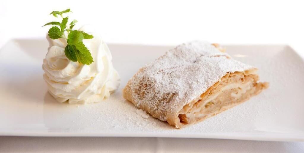 A dessert consisting of a pastry and whipped cream, dusted with powdered sugar, accompanied by a mint leaf.