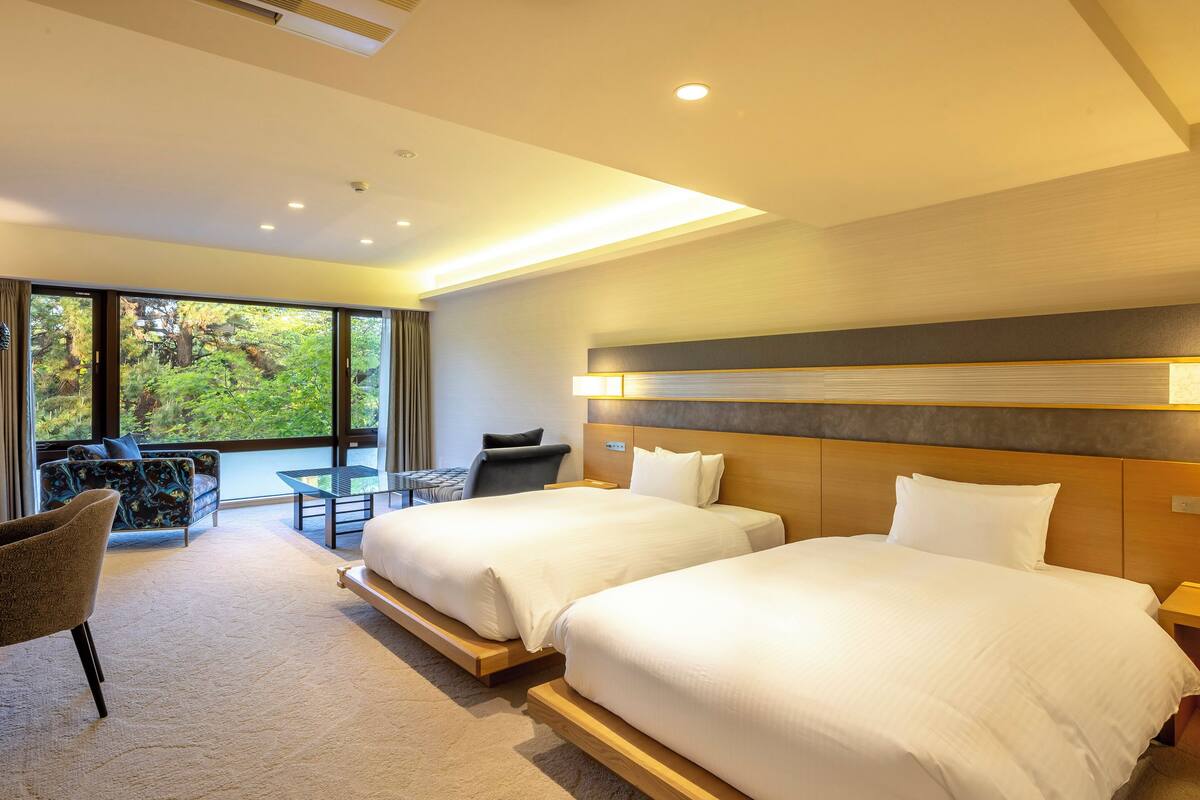A hotel room with two beds, a sofa, a small table, and a chair.