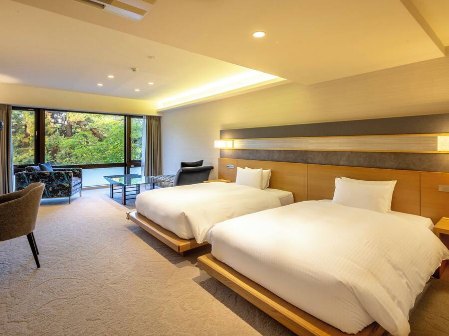 A hotel room with two beds, a sofa, a small table, and a chair.