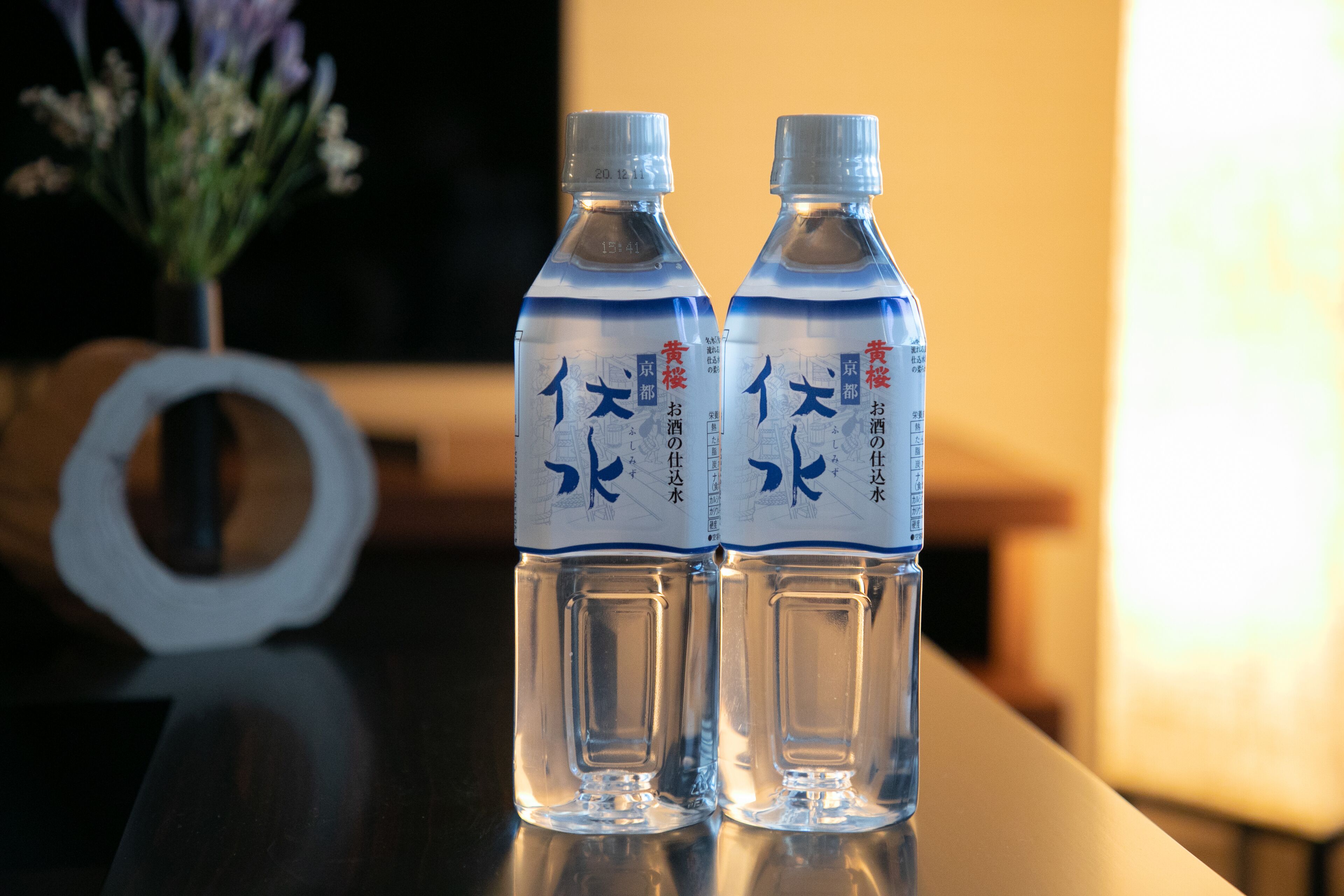 Zwei klare Wasserflaschen mit Etiketten auf einer spiegelnden Oberfläche.