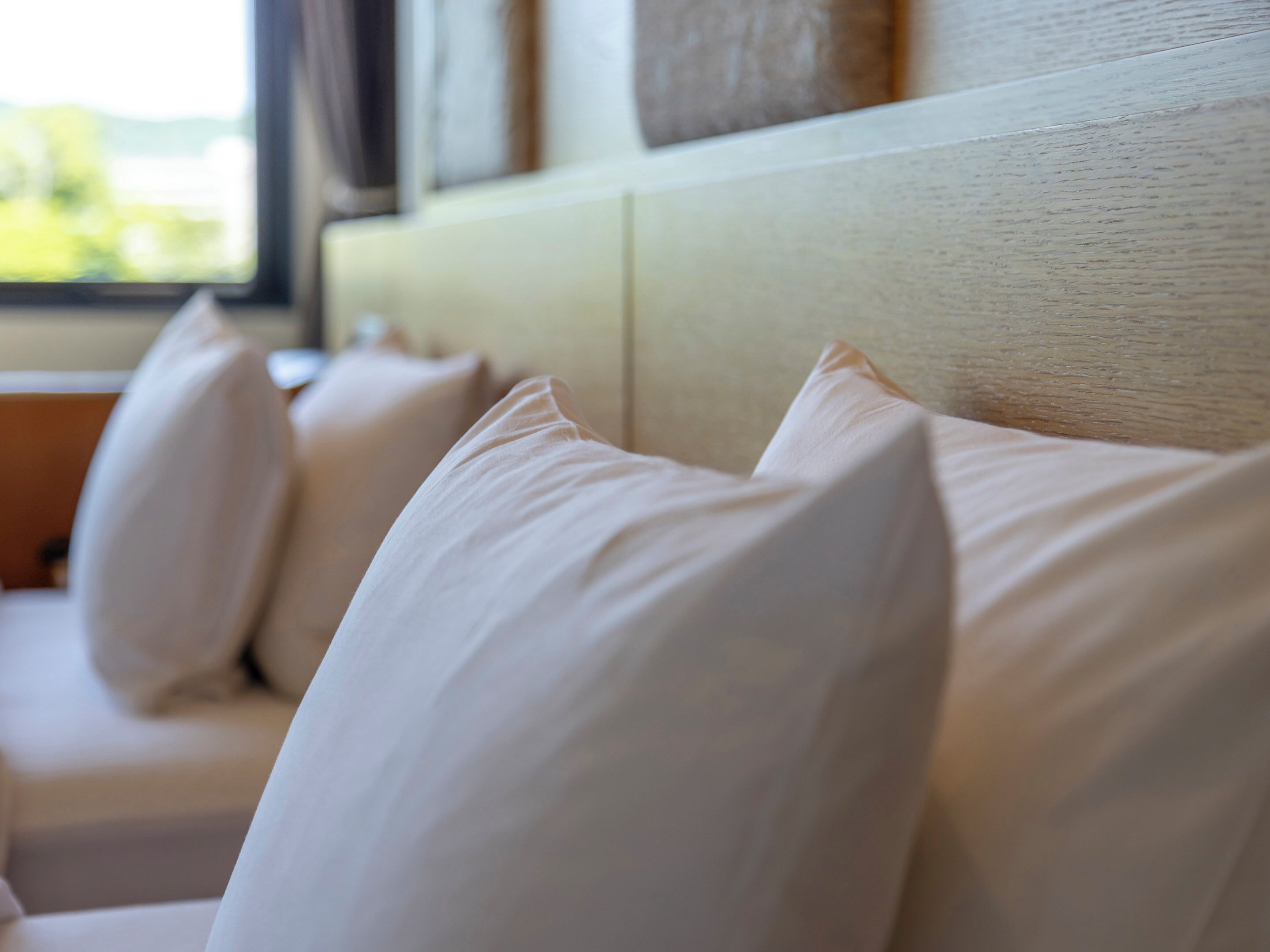 A row of white pillows on a beige headboard.