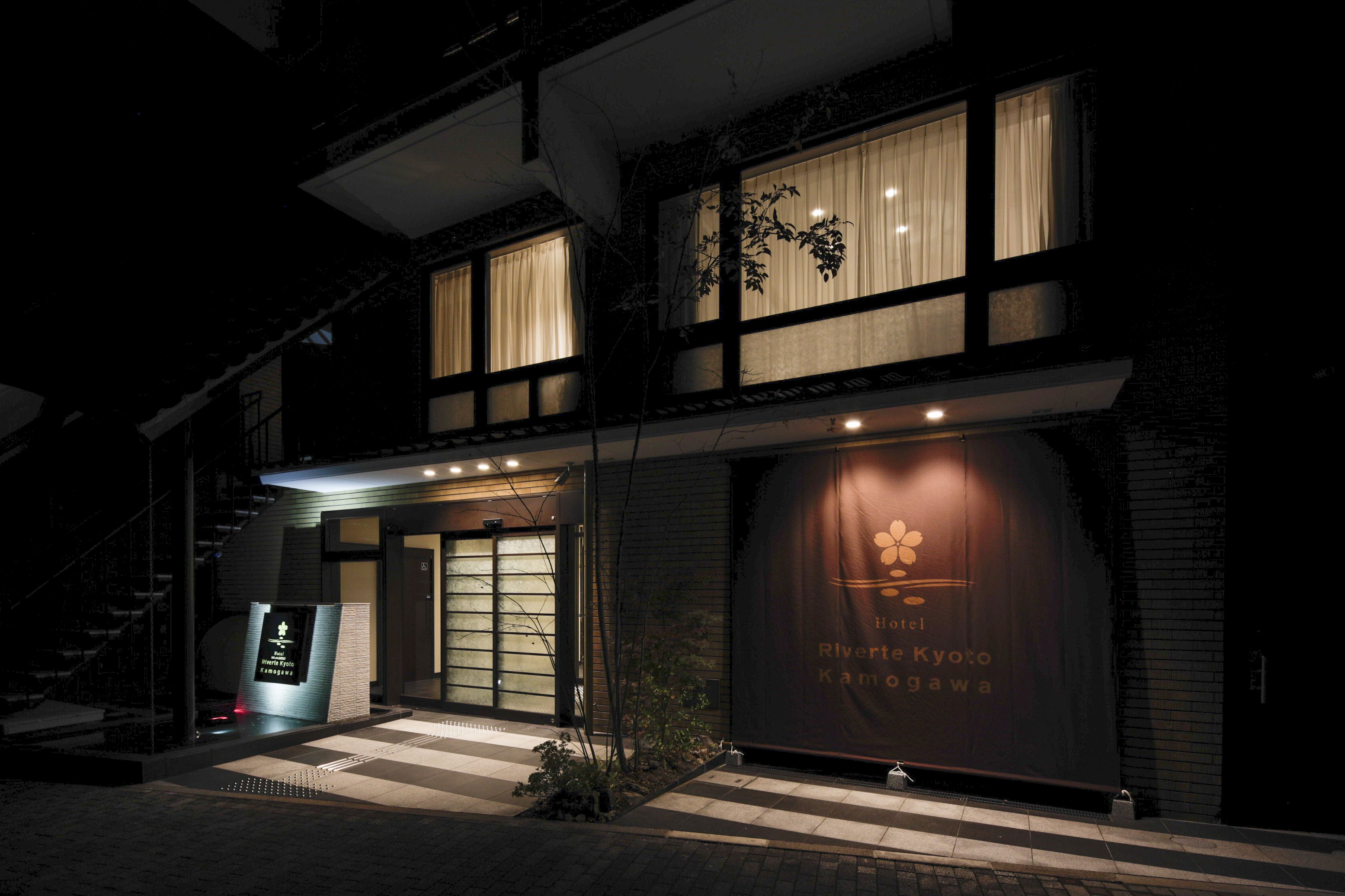 A hotel entrance with a large illuminated sign, a staircase, and a view of the building's facade.
