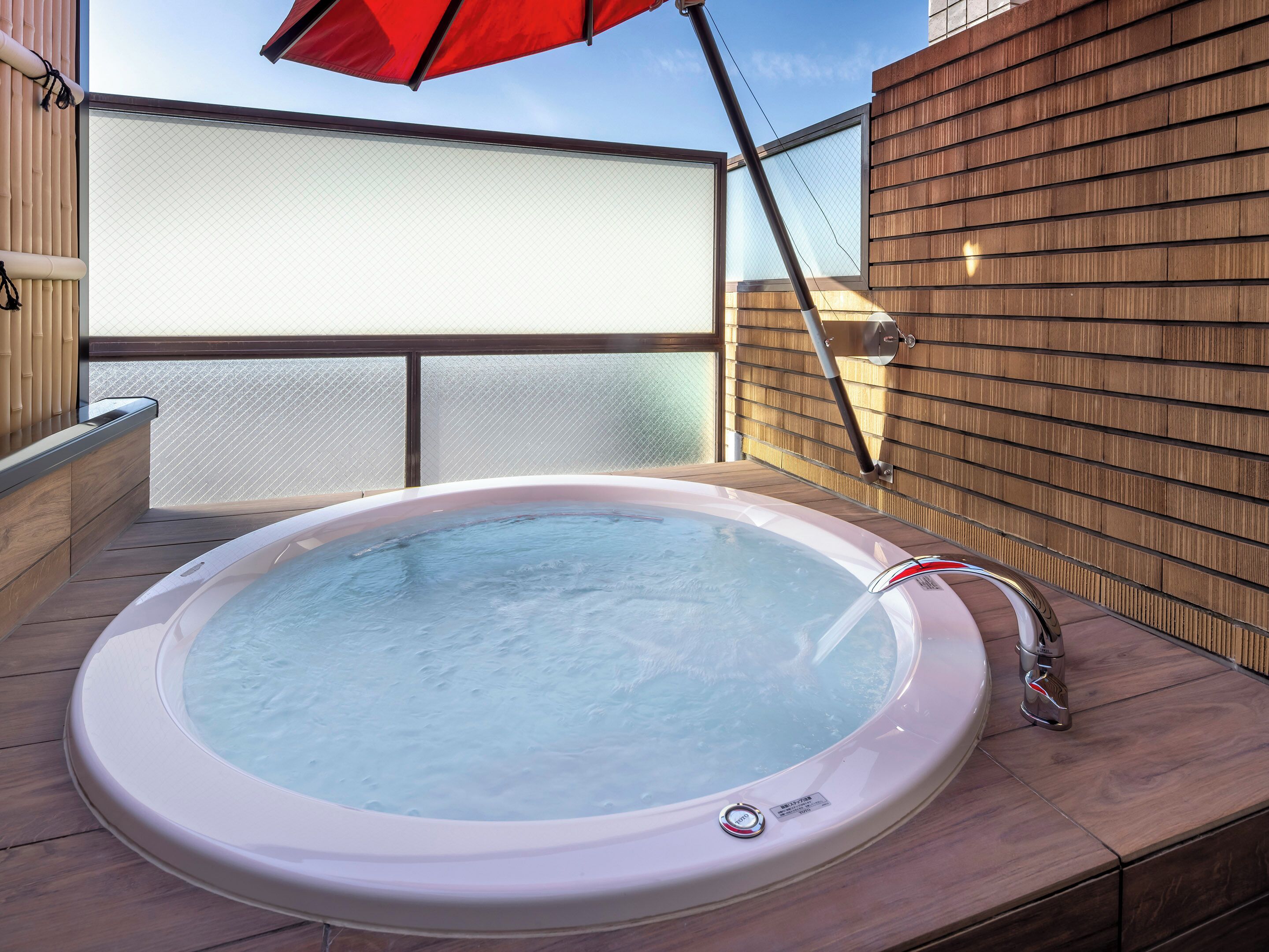 A hot tub on a wooden deck with a glass balustrade and a red umbrella.