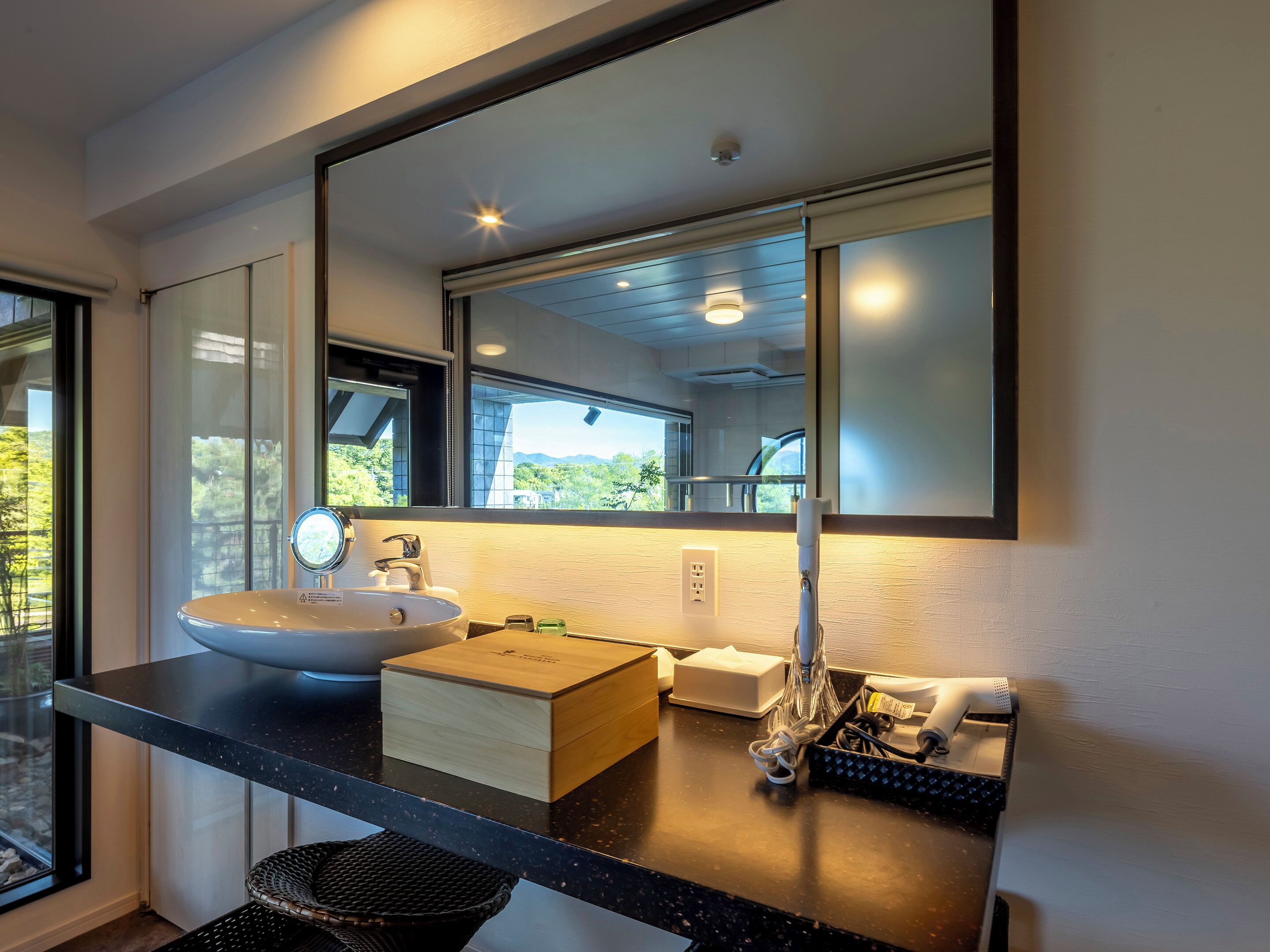 A modern bathroom with a large mirror, a sink, and a countertop with various toiletries.
