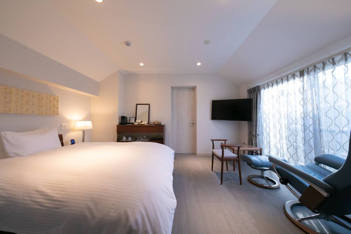 A hotel room with a large bed, a desk with a chair, a television, and a window with curtains.