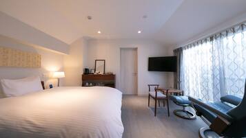 A hotel room with a large bed, a desk with a chair, a television, and a window with curtains.
