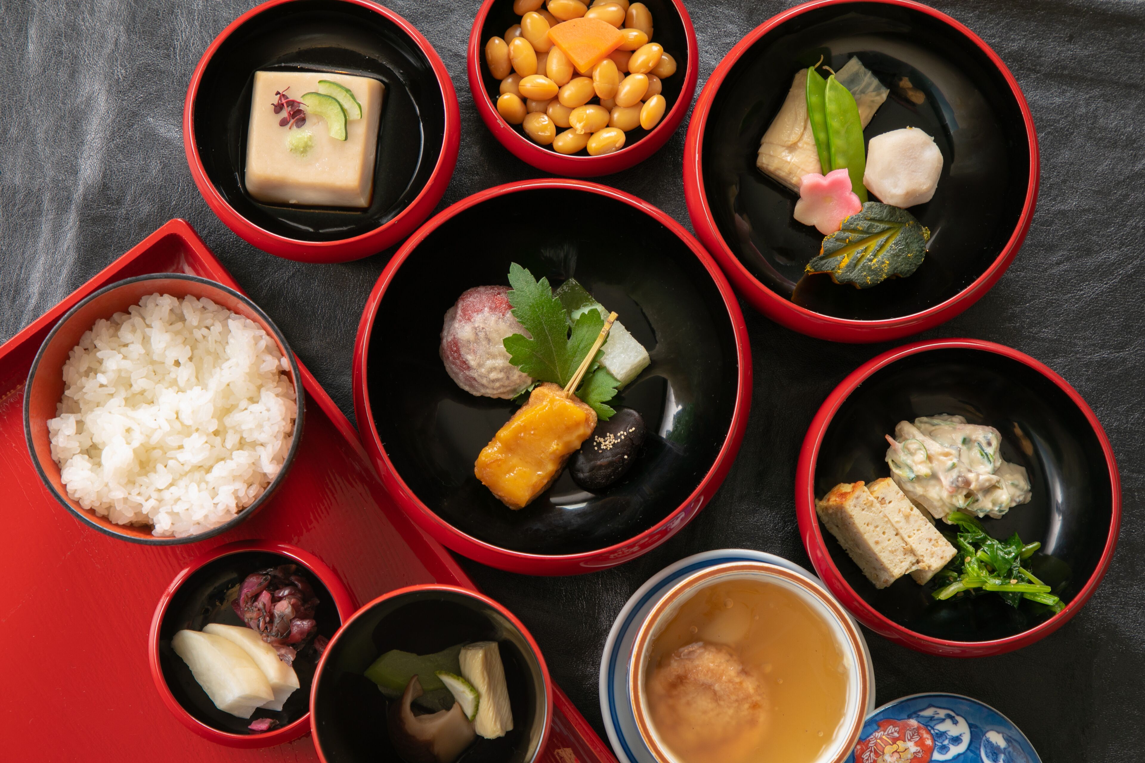 Diversitat de plats tradicionals japonesos presentats en bols vermells i negres sobre una taula.