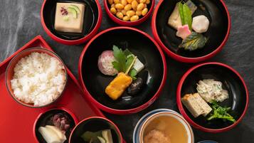 Diversitat de plats tradicionals japonesos presentats en bols vermells i negres sobre una taula.