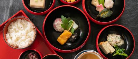 A variety of traditional Japanese dishes arranged in red and black bowls on a table.
