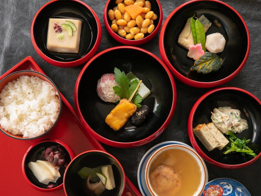 Diversitat de plats tradicionals japonesos presentats en bols vermells i negres sobre una taula.