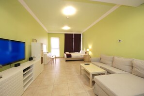 A modern living room with a flat-screen TV, a sofa, a coffee table, and a bed with a nightstand. - Signature Holiday Home - Venetian (Dubai)