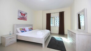 A bedroom with a bed, nightstand, dresser, and a painting on the wall. - Signature Holiday Home - Red Residence (Dubai)