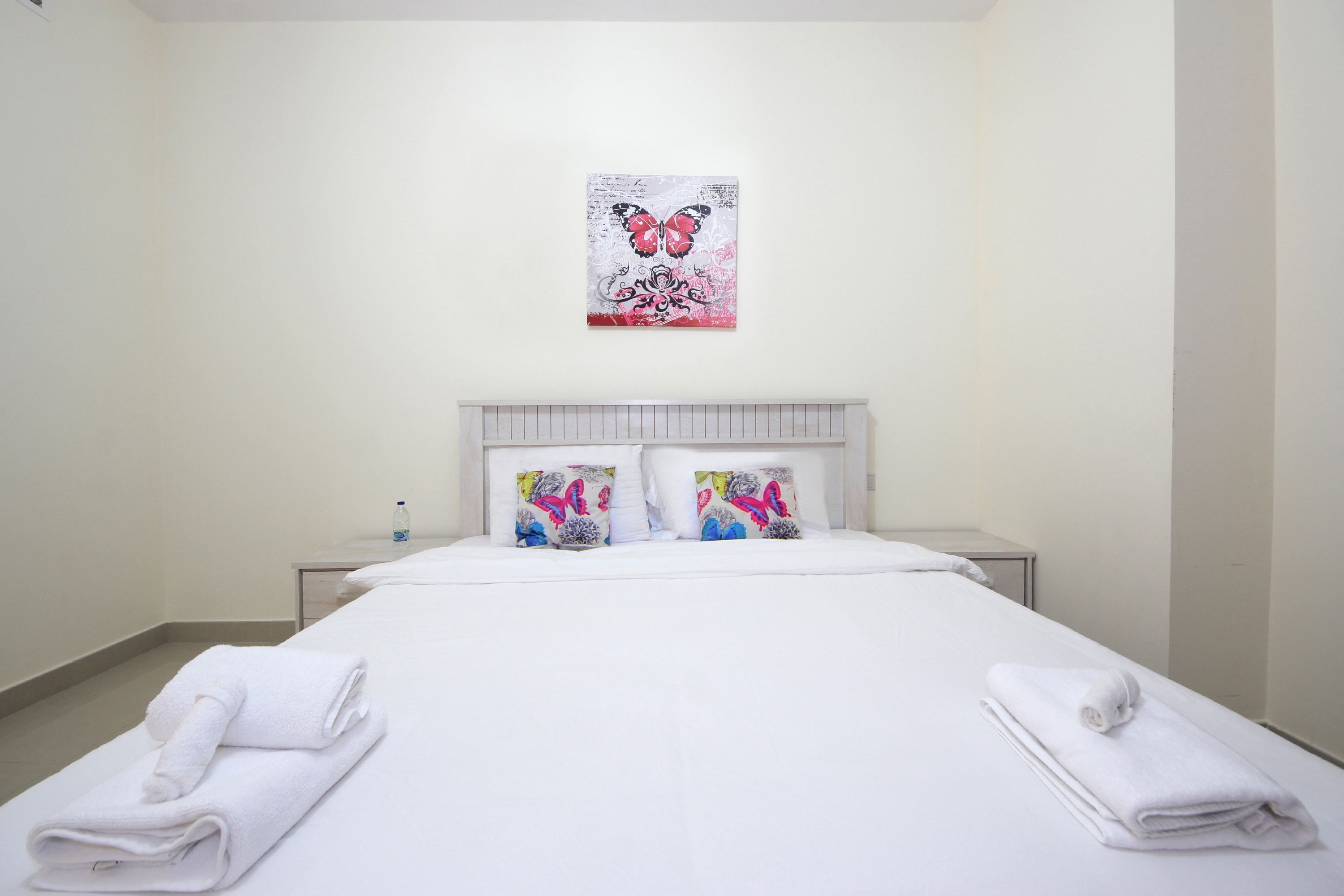 A hotel room with a bed, white towels, two decorative pillows, a bedside table, and a wall-mounted artwork.