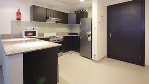A compact kitchen with dark cabinets, a microwave, a stove, and a refrigerator. - Signature Holiday Home - Red Residence (Dubai)