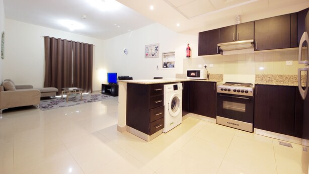 A modern kitchen with a built-in washer and oven, a dining area with a sofa, and a living room with a TV. - Signature Holiday Home - Red Residence (Dubai)