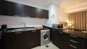 A compact kitchen with dark cabinets, a built-in washing machine, a sink, and a coffee maker. - Signature Holiday Home - Matrix Tower (Dubai)