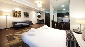 A hotel room with a bed, a sofa, a desk, a mirror, and a kitchenette. - Signature Holiday Home - Matrix Tower (Dubai)