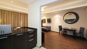 A modern hotel room with a kitchenette, a dining area with a round mirror, and a seating area with a sofa and chairs. - Signature Holiday Home - Matrix Tower (Dubai)