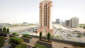 A high-rise building with multiple balconies, surrounded by a parking lot and greenery. - Signature Holiday Home - Matrix Tower (Dubai)