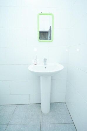 A bathroom with a white sink, a green-framed mirror, and a white toilet. - OYO 1239 Mojokerto Classic Homestay (Mojokerto)