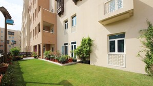 A courtyard with a well-maintained lawn, potted plants, and a building with multiple balconies and windows.