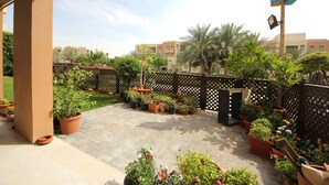 A patio area with potted plants, a wooden fence, and buildings in the background.