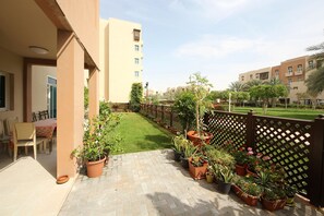 A courtyard with a paved walkway, potted plants, a lawn, and a wooden fence.
