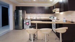 Una cocina moderna con armarios oscuros, electrodomésticos de acero inoxidable, lavadora y una zona de bar con taburetes.