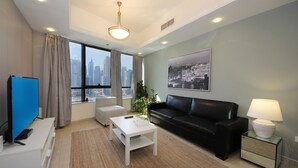 Una sala de estar moderna con un sofá de cuero negro, una mesa de centro blanca, un televisor y vistas a la ciudad a través de amplias ventanas.