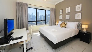 Una habitación de hotel con una cama, un escritorio con computadora, una silla, una mesita de noche con lámpara y cuadros en la pared.