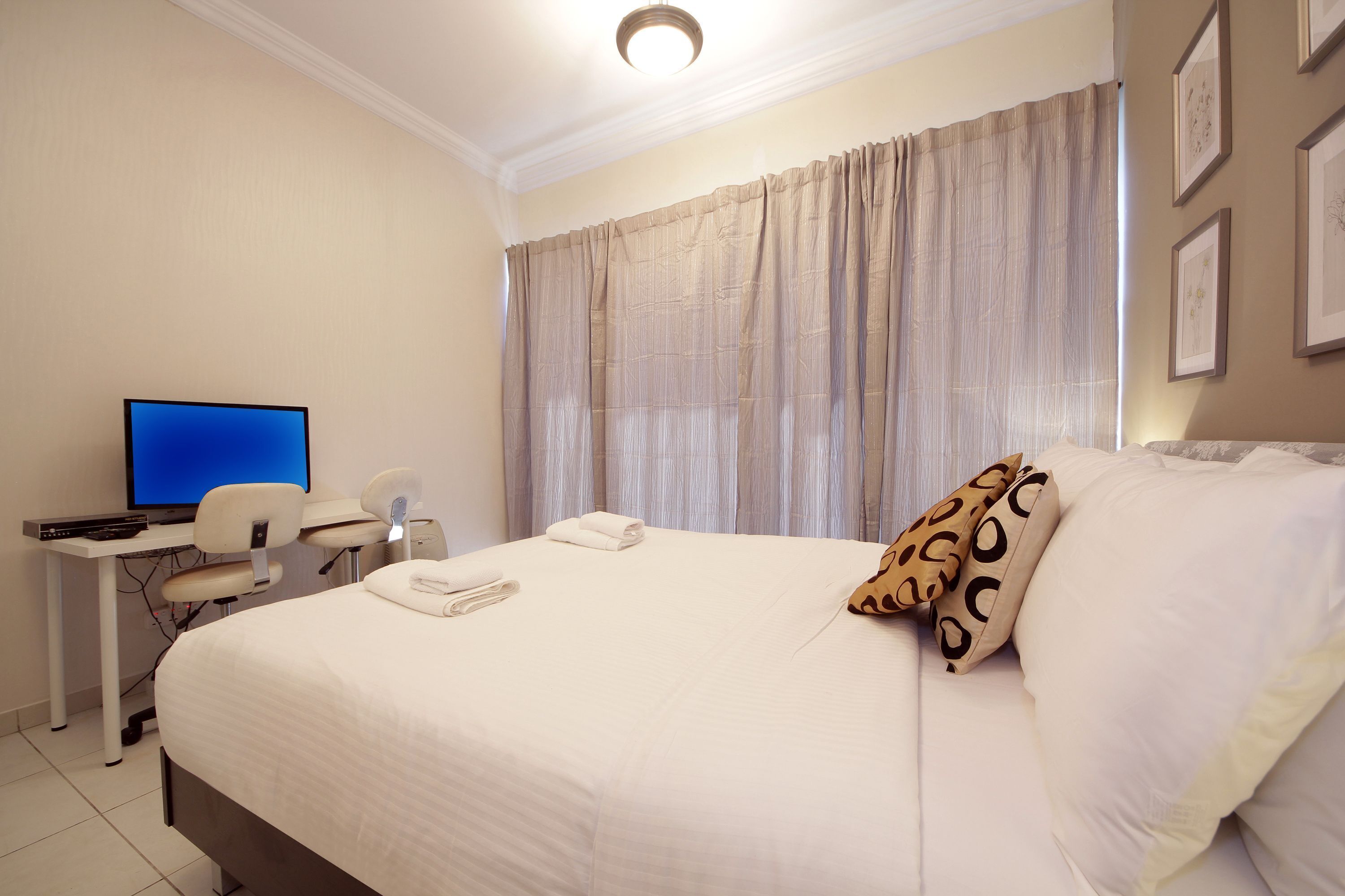 Ein Hotelzimmer mit Bett, Schreibtisch mit Computer und einem Fenster mit Vorhängen.