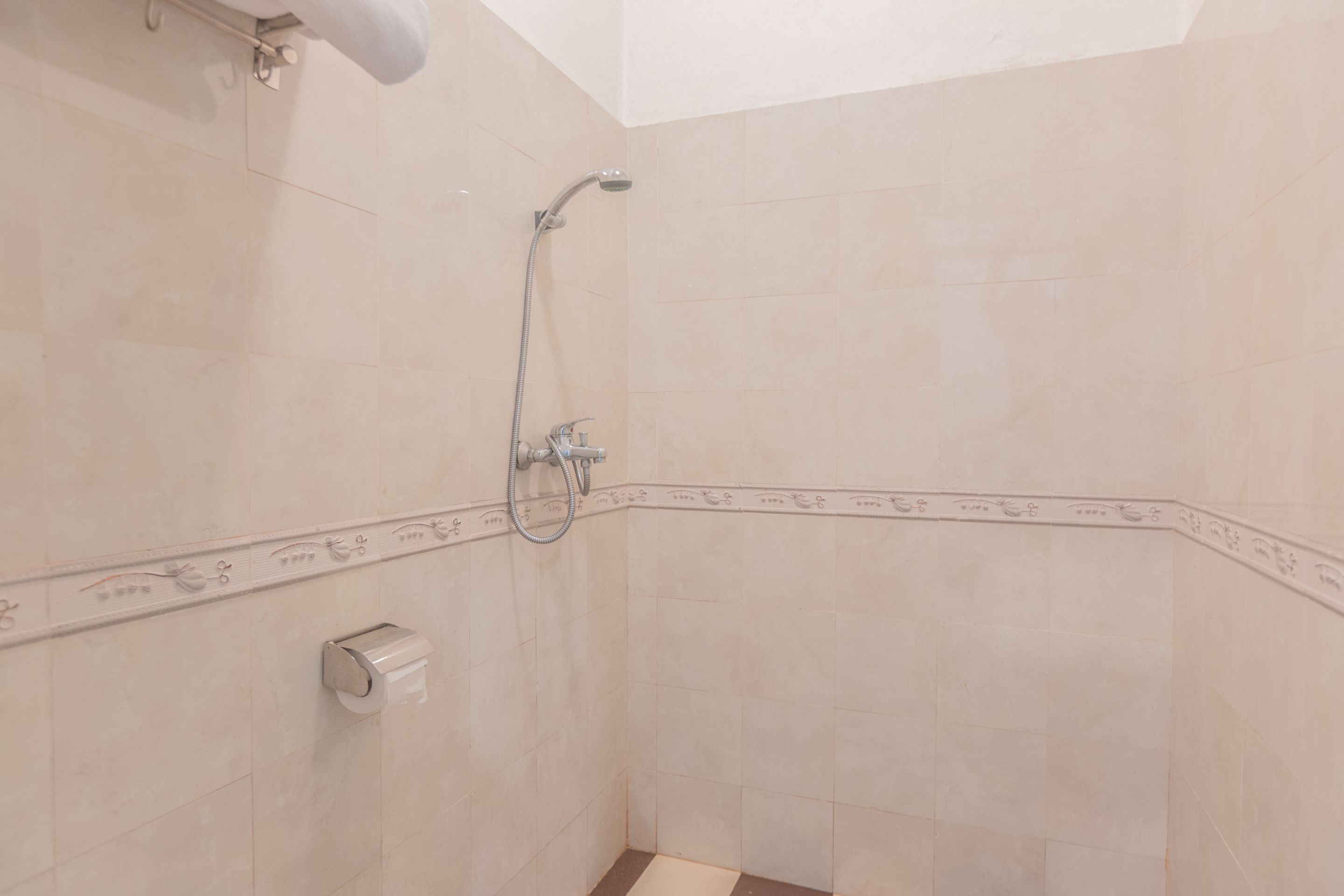 A corner of a bathroom with beige tiles, a showerhead, a towel rack, and a toilet paper holder.