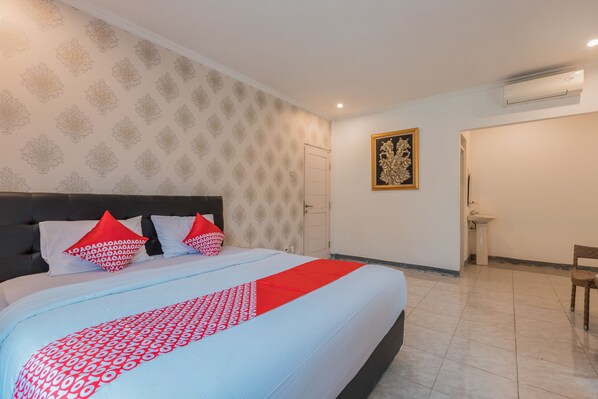 A hotel room with a large bed, a headboard, a wall-mounted air conditioner, a door, a small table, and a chair.