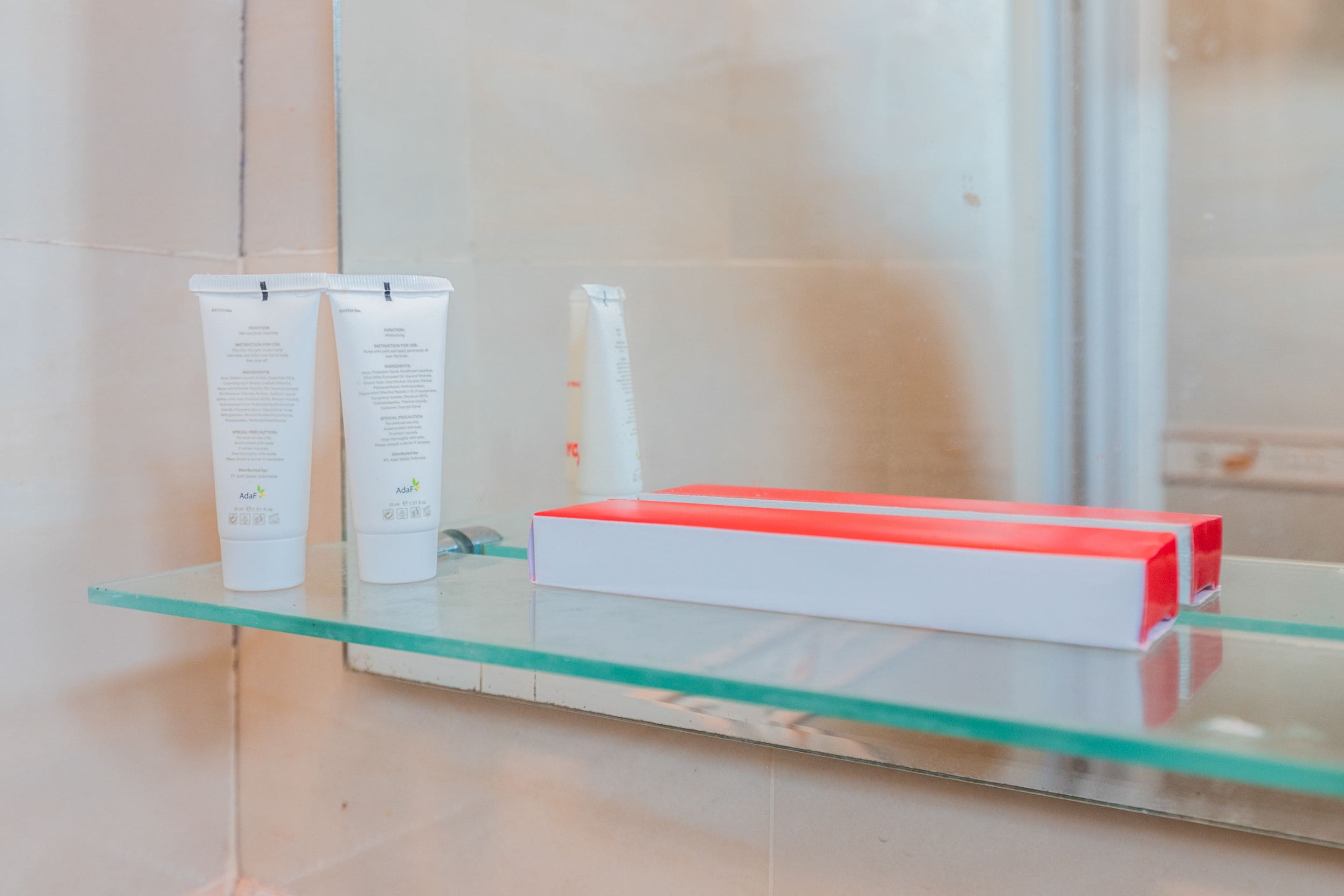 A bathroom with a glass shelf holding toiletries and a red box.