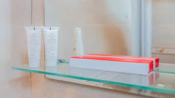A bathroom with a glass shelf holding toiletries and a red box.