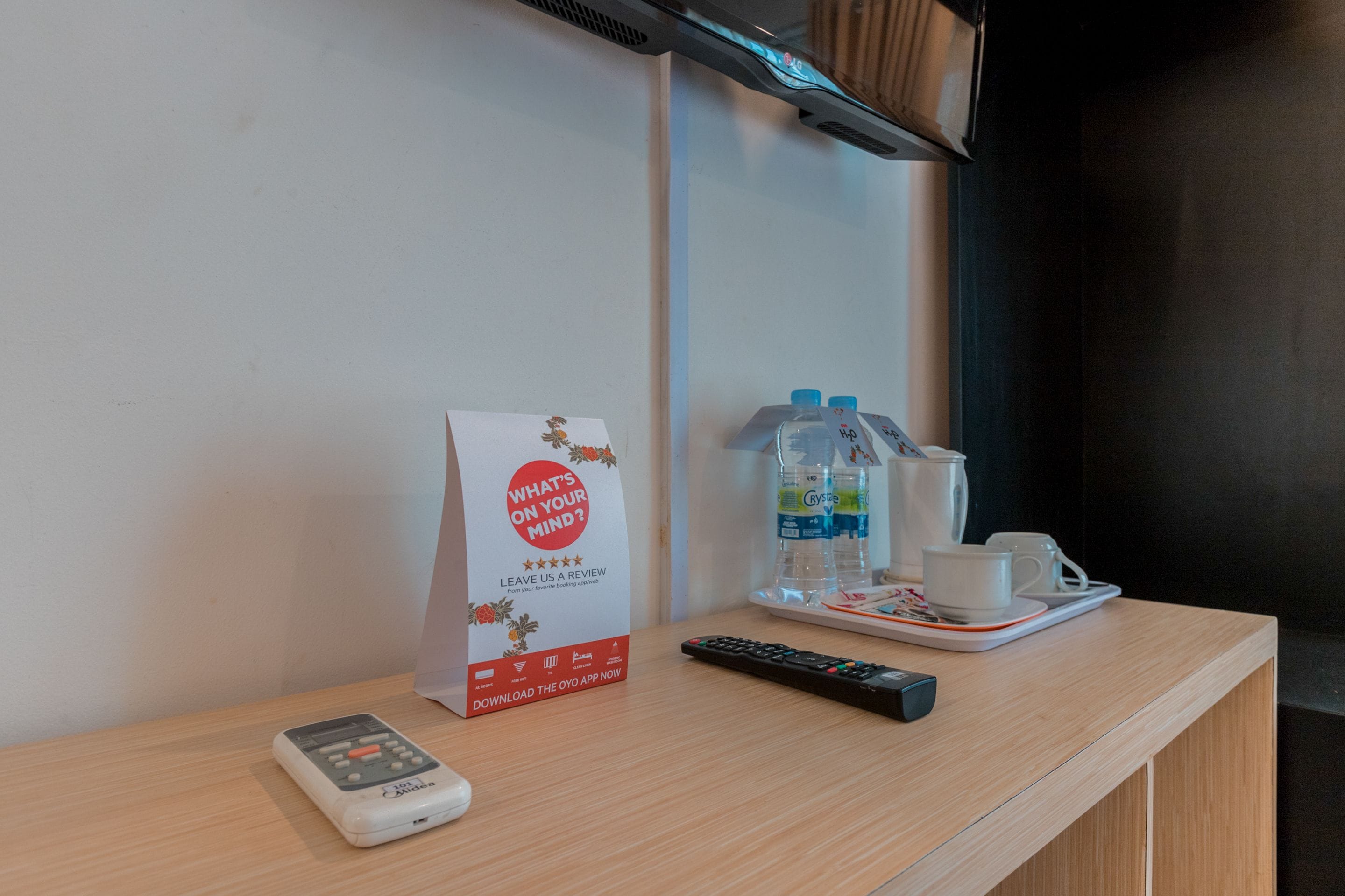 Mostrador de recepción de hotel con un control remoto, una botella de agua, una taza y un cartel que promociona una aplicación de reseñas.