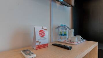 Mostrador de recepción de hotel con un control remoto, una botella de agua, una taza y un cartel que promociona una aplicación de reseñas.