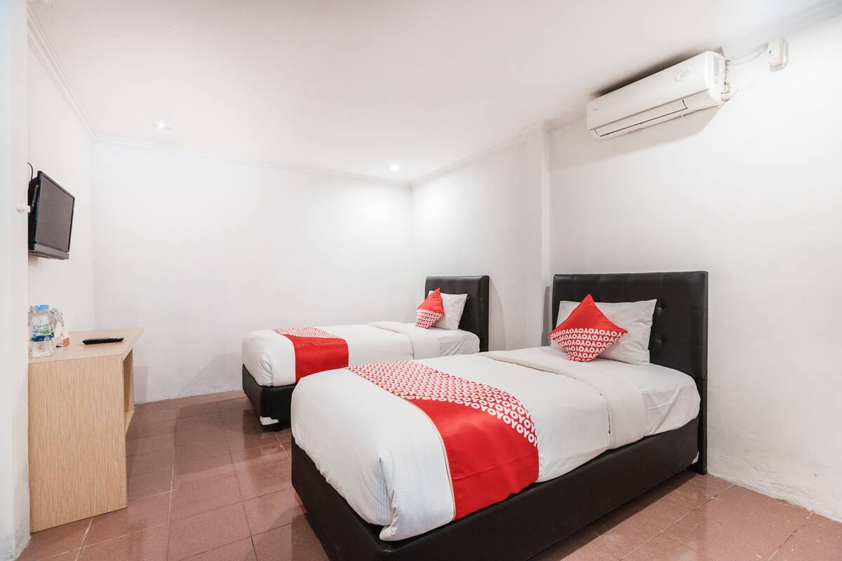 A hotel room with two beds, a wooden nightstand, a TV, and an air conditioning unit.