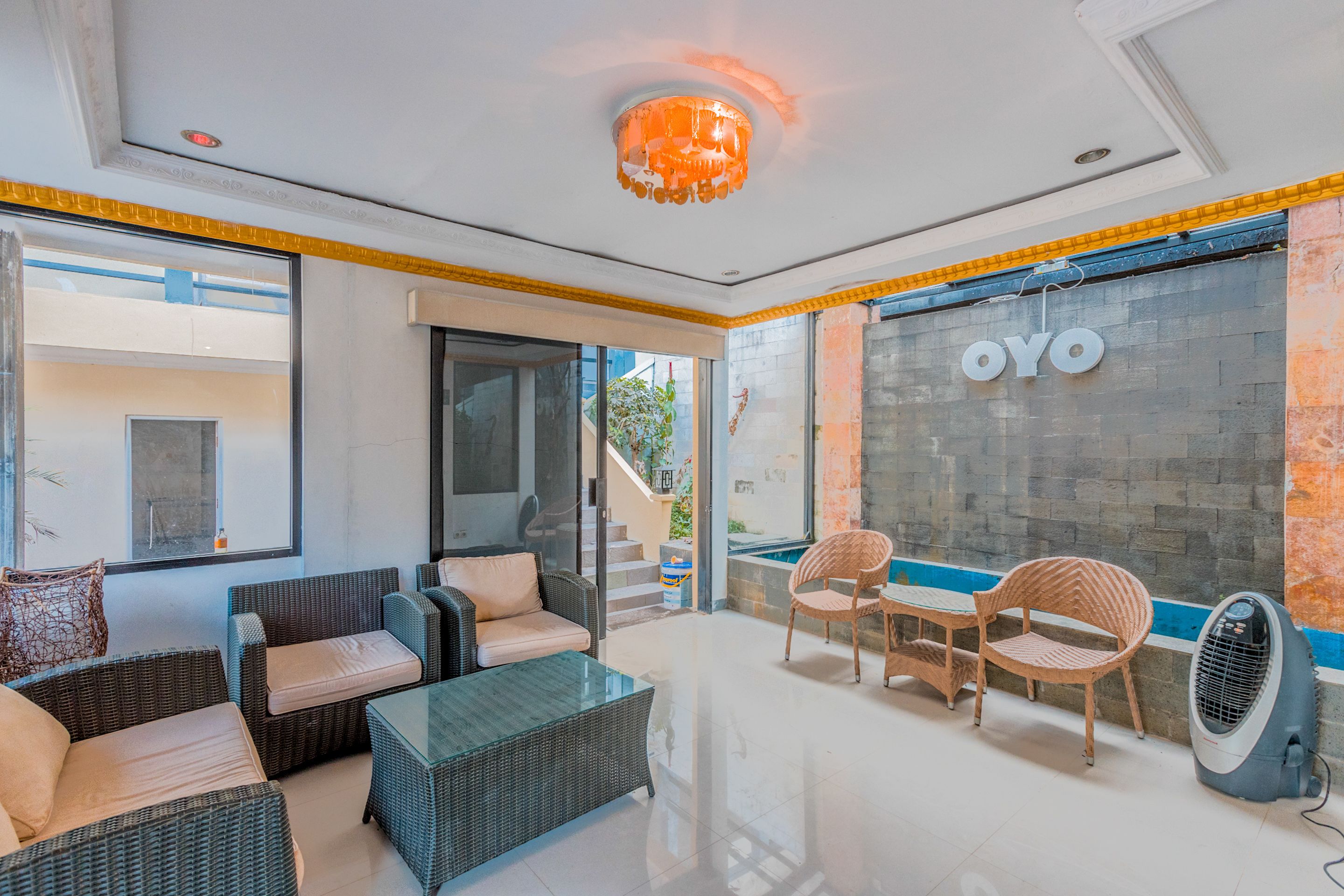 Un espace de détente moderne, avec des meubles en osier, une table basse en verre et un ventilateur fixé au mur.