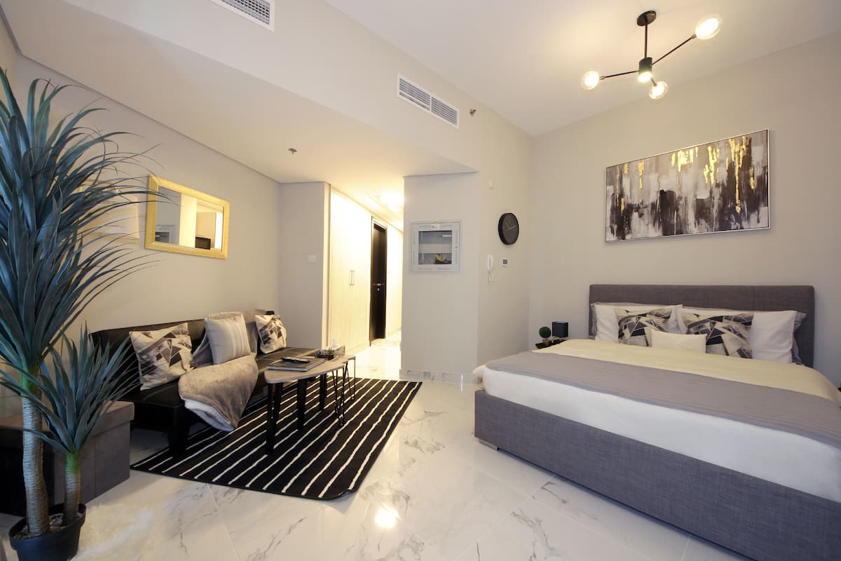 A modern bedroom with a large bed, a sofa, a dining table, and a potted plant.