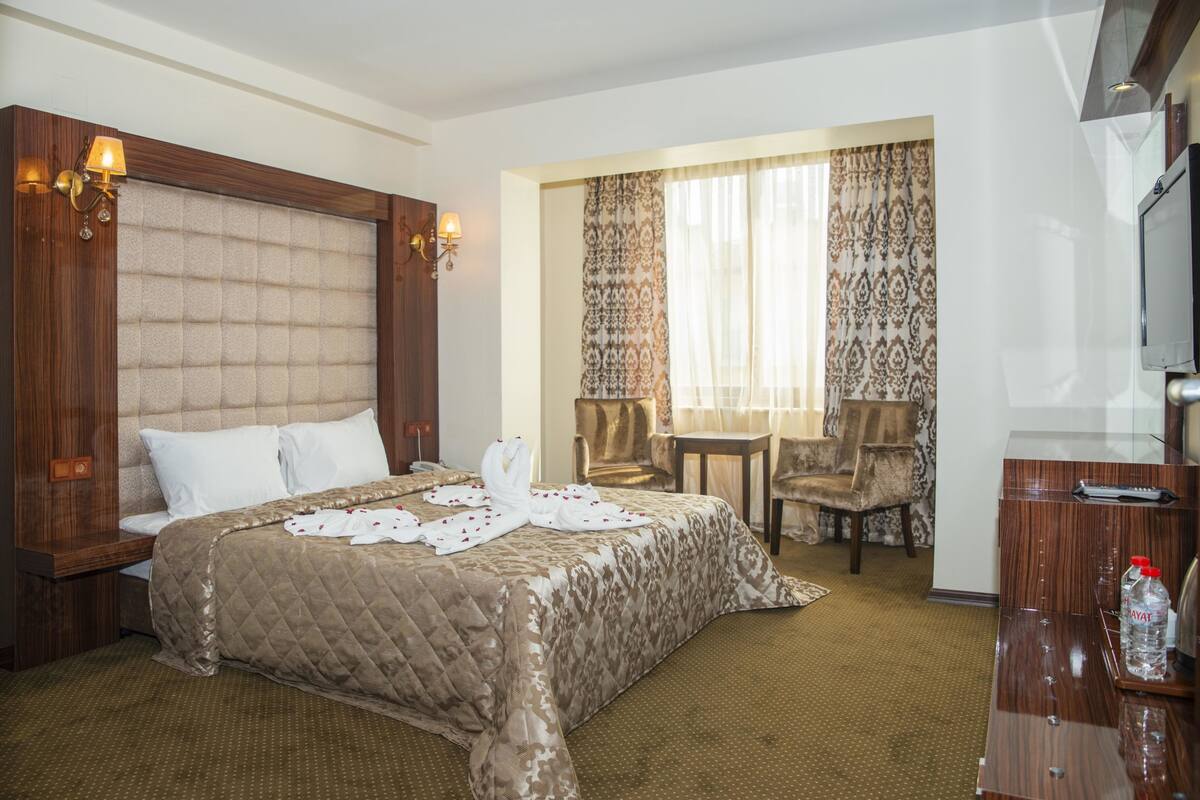 A hotel room with a large bed, a desk with a chair, a television, and a window with curtains.