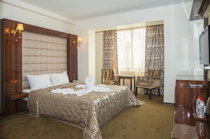 Une chambre d’hôtel avec un grand lit, un bureau avec une chaise, une télévision et une fenêtre avec des rideaux.