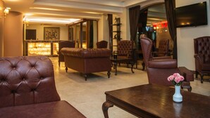 A hotel lobby with leather sofas, a wooden coffee table, and a TV mounted on the wall. - Neccar Otel (Antakya)