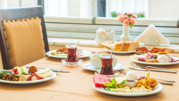 A table set with various dishes, including plates of food, a glass of tea, and a vase with flowers. - Neccar Otel (Antakya)
